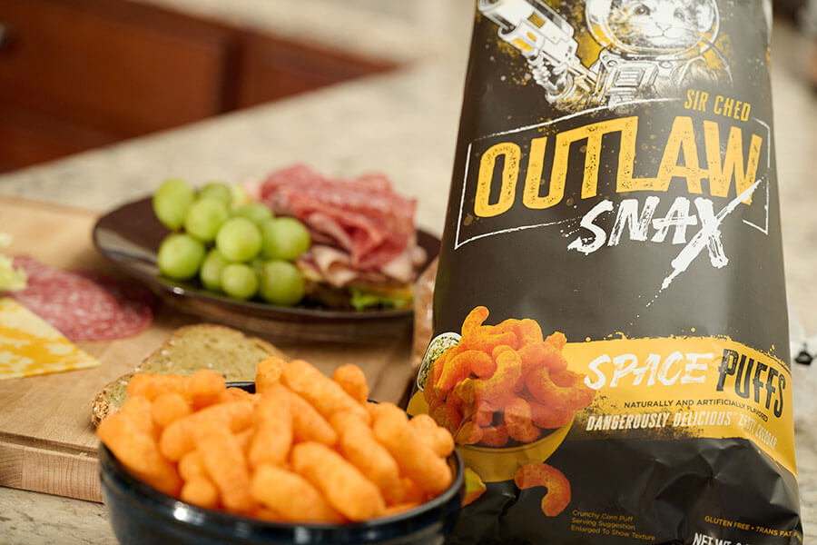 Outlaw Snax Space Puffs cheese snacks served with a charcuterie board and fresh fruit.